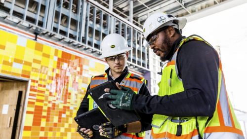 Image of two PCL construction workers on iPads discussing safety procedures.