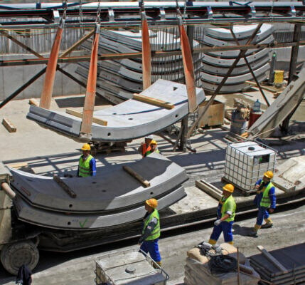 Construction workers on a job site walking close to heavy hanging concrete pieces while guiding it safety.